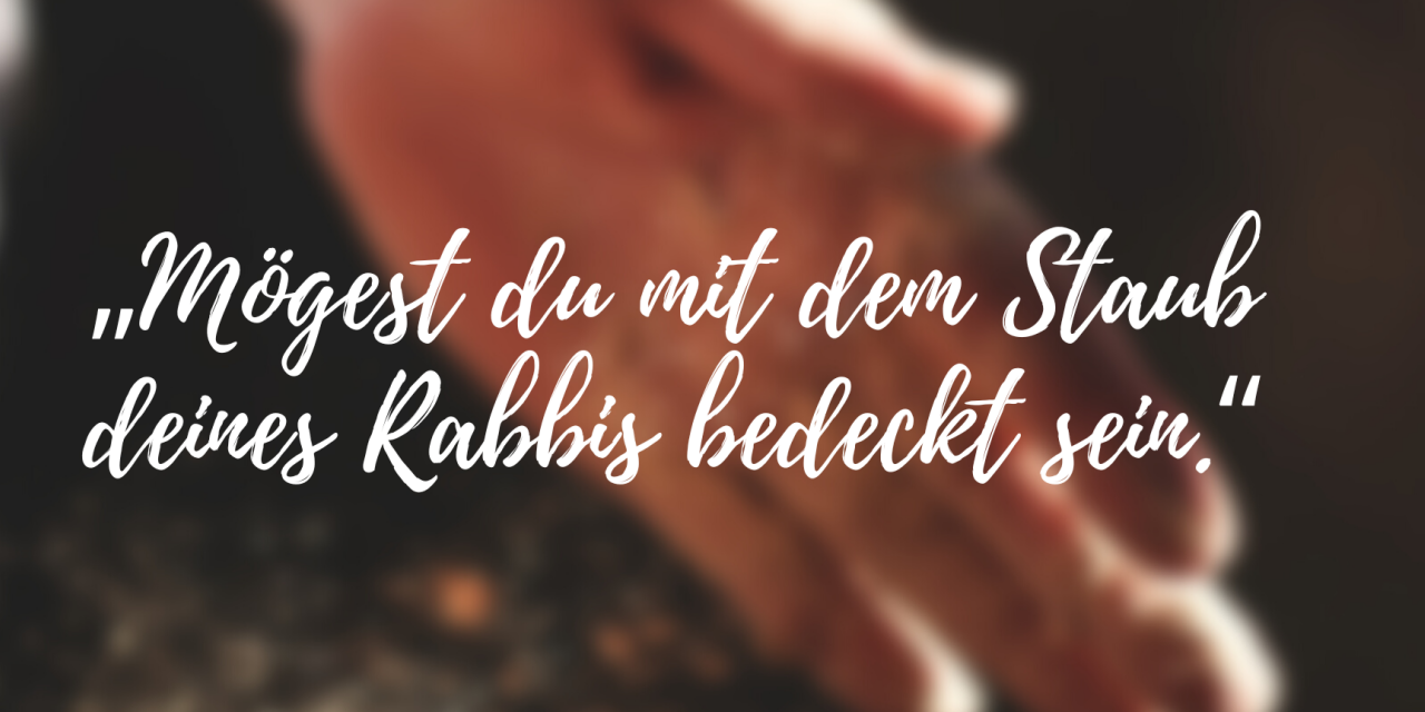 Text „Mögest du mit dem Staub deines Rabbis bedeckt sein.“. Im Hintergrund Hände mit Staub